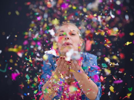 beautiful young woman celebrating new year and chrismas party while blowing confetti decorations to camera isolated over gray background