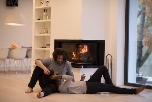 beautiful young multiethnic couple using tablet computer on the floor of their luxury home in front of fireplace at autumn day