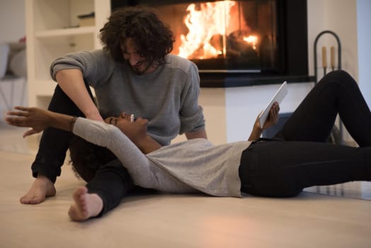 beautiful young multiethnic couple using tablet computer on the floor of their luxury home in front of fireplace at autumn day