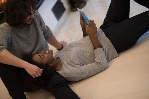 beautiful young multiethnic couple using tablet computer on the floor of their luxury home in front of fireplace at autumn day