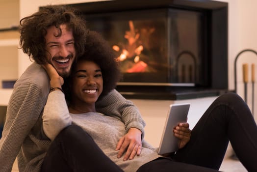 beautiful young multiethnic couple using tablet computer on the floor of their luxury home in front of fireplace at autumn day