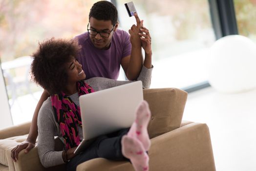 Happy young african american couple shopping online through laptop using credit card at home