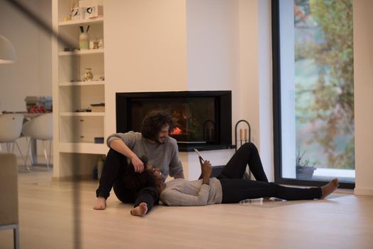 beautiful young multiethnic couple using tablet computer on the floor of their luxury home in front of fireplace at autumn day