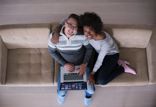 Young multiethnic couple relaxes in the luxury living room, using a laptop computer top view