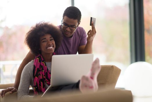 Happy young african american couple shopping online through laptop using credit card at home