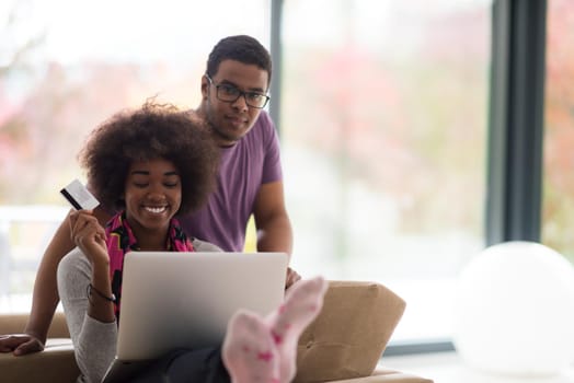 Happy young african american couple shopping online through laptop using credit card at home