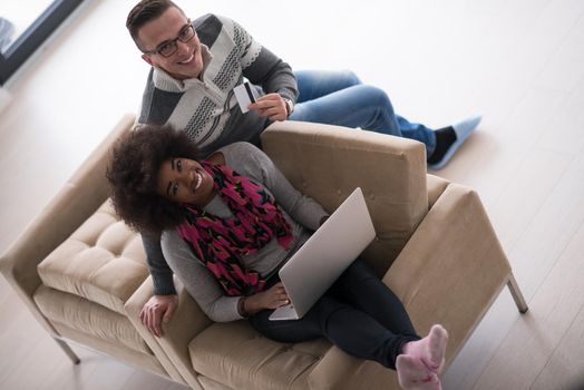 Happy young multiethnic couple shopping online through laptop using credit card at home