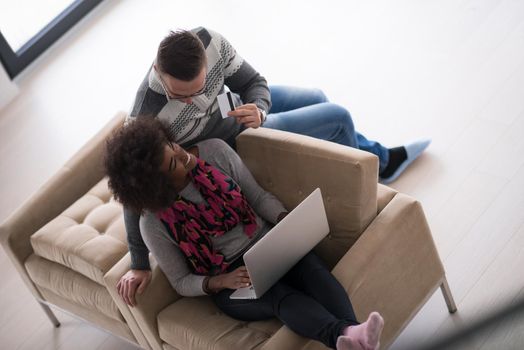 Happy young multiethnic couple shopping online through laptop using credit card at home