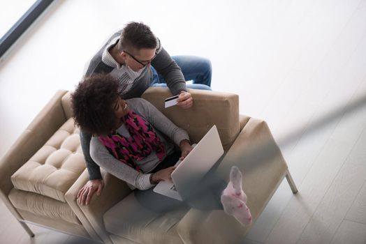 Happy young multiethnic couple shopping online through laptop using credit card at home