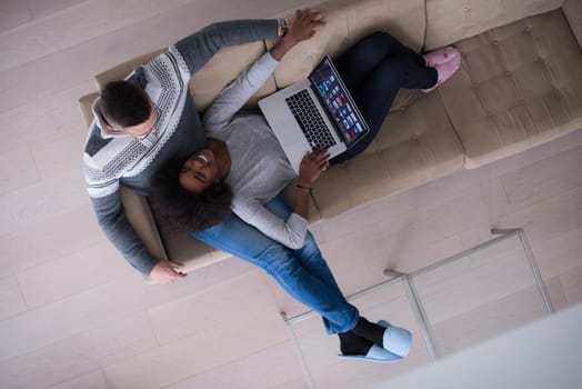 Young multiethnic couple relaxes in the luxury living room, using a laptop computer top view