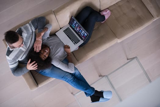 Young multiethnic couple relaxes in the luxury living room, using a laptop computer top view