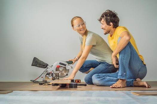 Married couple installing new wooden laminate flooring on a warm film floor. Infrared floor heating system under laminate floor.