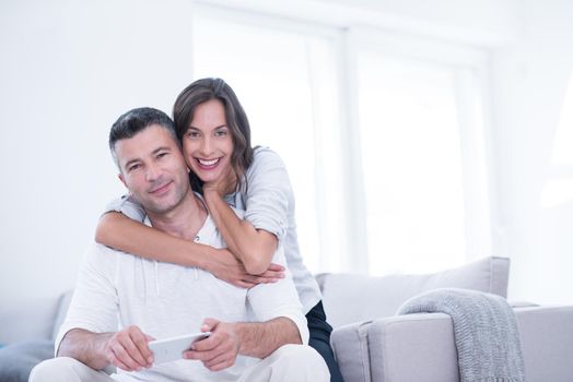 Young happy couple using mobile phone at home together, looking at screen, smiling.