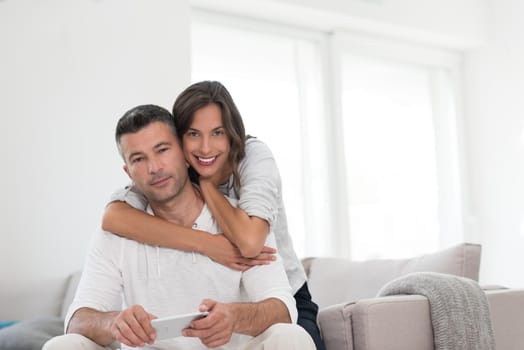 Young happy couple using mobile phone at home together, looking at screen, smiling.