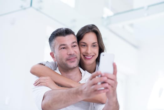 Young happy couple using mobile phone at home together, looking at screen, smiling.