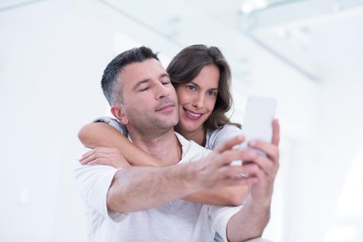 Young happy couple using mobile phone at home together, looking at screen, smiling.