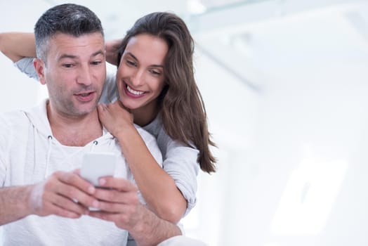 Young happy couple using mobile phone at home together, looking at screen, smiling.