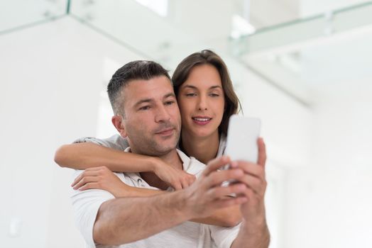 Young happy couple using mobile phone at home together, looking at screen, smiling.