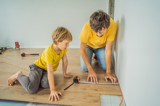 Father and son installing new wooden laminate flooring on a warm film floor. Infrared floor heating system under laminate floor.