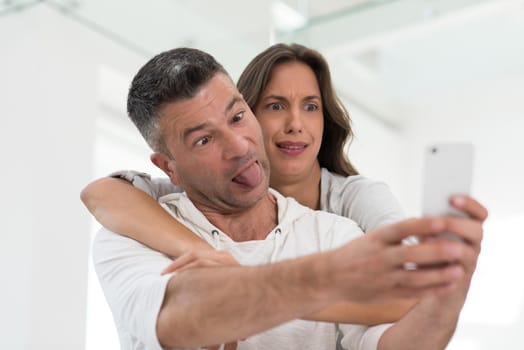 Young happy couple using mobile phone at home together, looking at screen, smiling.