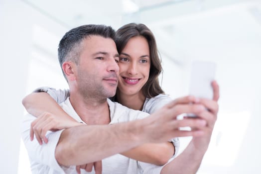 Young happy couple using mobile phone at home together, looking at screen, smiling.