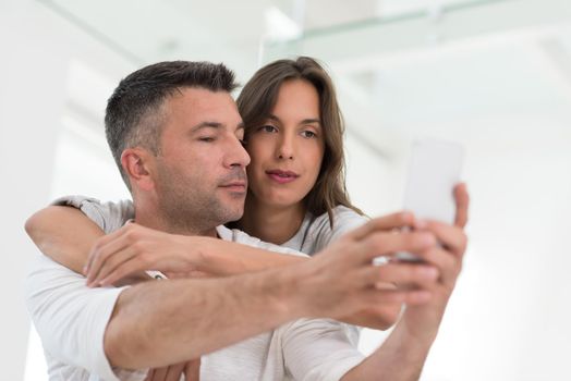 Young happy couple using mobile phone at home together, looking at screen, smiling.