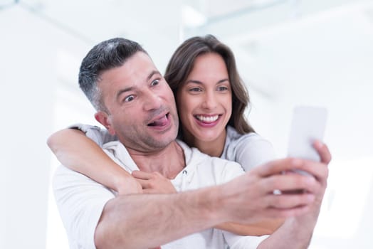 Young happy couple using mobile phone at home together, looking at screen, smiling.