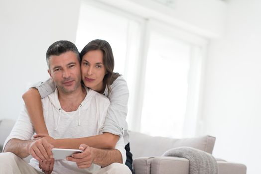 Young happy couple using mobile phone at home together, looking at screen, smiling.