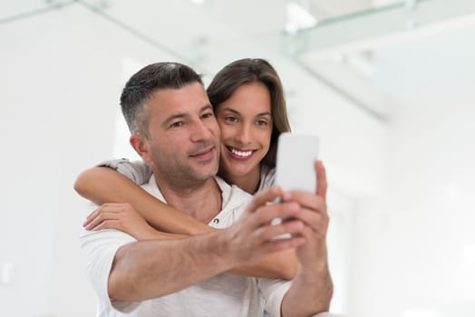 Young happy couple using mobile phone at home together, looking at screen, smiling.