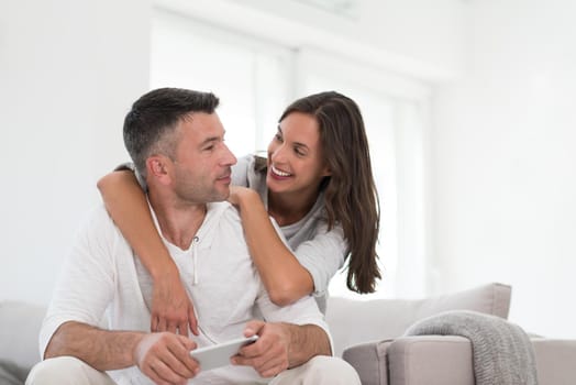 Young happy couple using mobile phone at home together, looking at screen, smiling.