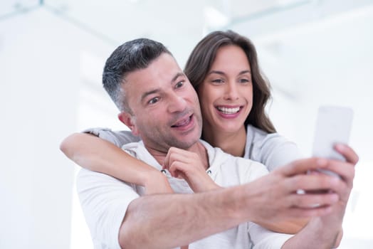 Young happy couple using mobile phone at home together, looking at screen, smiling.