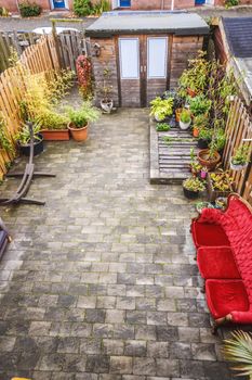 Cozy courtyard of a house with pots of flowers and a bright scarlet velvet sofa