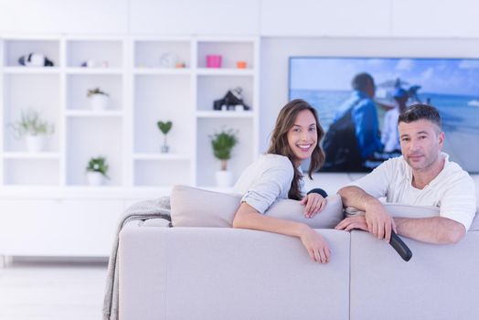 Young couple on the sofa watching television together in their luxury home