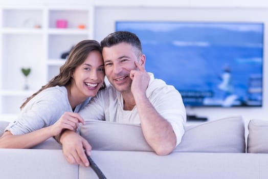 Young couple on the sofa watching television together in their luxury home