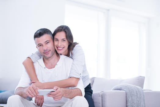 Young happy couple using mobile phone at home together, looking at screen, smiling.