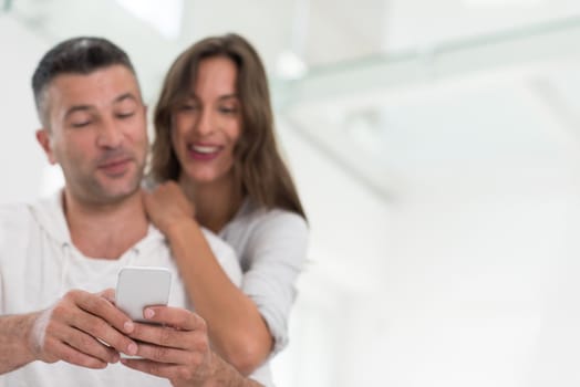 Young happy couple using mobile phone at home together, looking at screen, smiling.