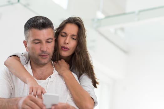 Young happy couple using mobile phone at home together, looking at screen, smiling.