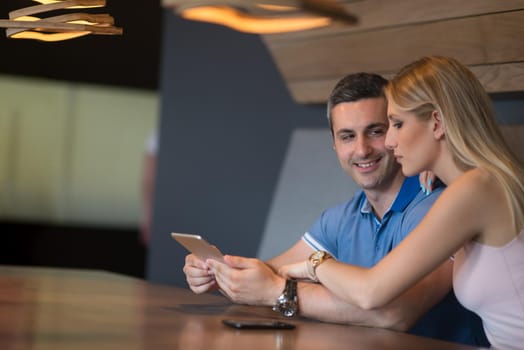 Young couple using tablet computer at luxury home together, looking at screen, smiling.