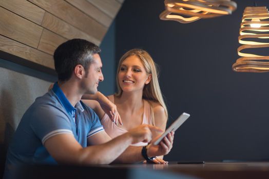 Young couple using tablet computer at luxury home together, looking at screen, smiling.