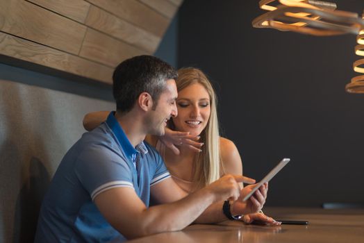 Young couple using tablet computer at luxury home together, looking at screen, smiling.