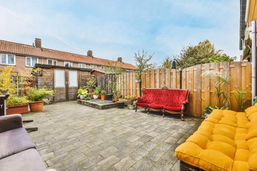 Cozy courtyard of a house with pots of flowers and a bright scarlet velvet sofa