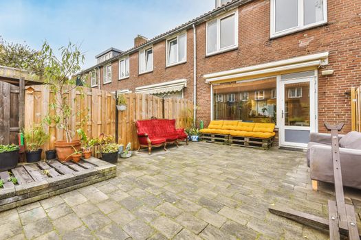 Cozy courtyard of a house with pots of flowers and a bright scarlet velvet sofa