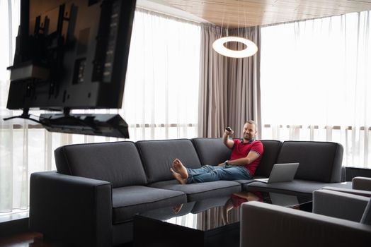 young handsome man enjoying free time watching television in his luxury home villa