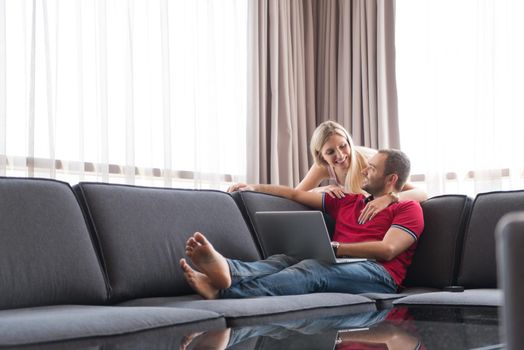 Young couple using laptop computer at luxury home together, looking at screen, smiling.