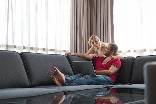 Young couple using laptop computer at luxury home together, looking at screen, smiling.