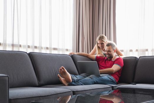 Young couple using laptop computer at luxury home together, looking at screen, smiling.