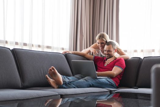 Young couple using laptop computer at luxury home together, looking at screen, smiling.