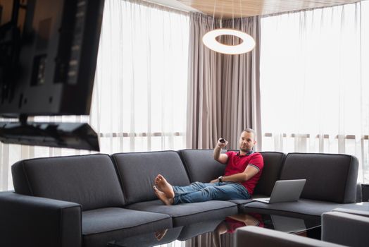 young handsome man enjoying free time watching television in his luxury home villa