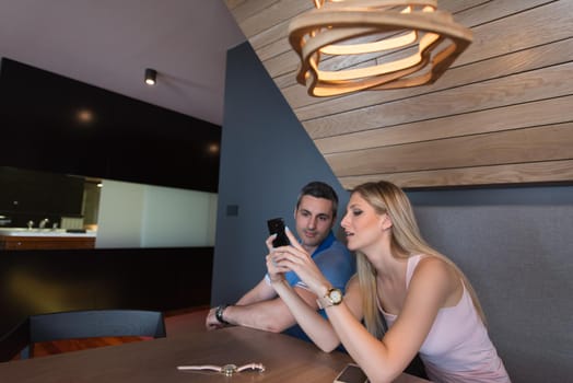 Young couple using mobile phone at luxury home together, looking at screen, smiling.