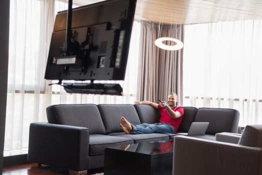 young handsome man enjoying free time watching television in his luxury home villa